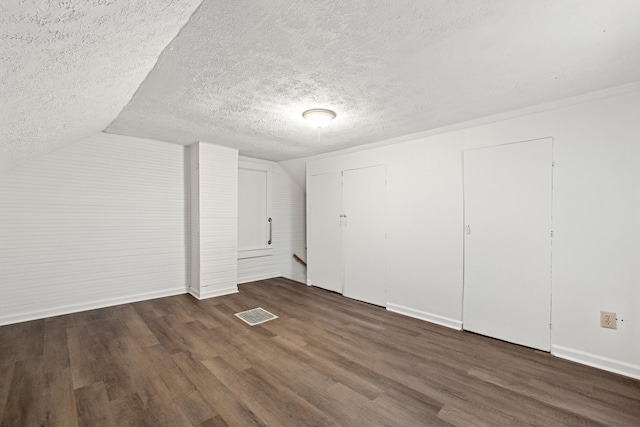 additional living space with a textured ceiling, vaulted ceiling, and dark wood-type flooring