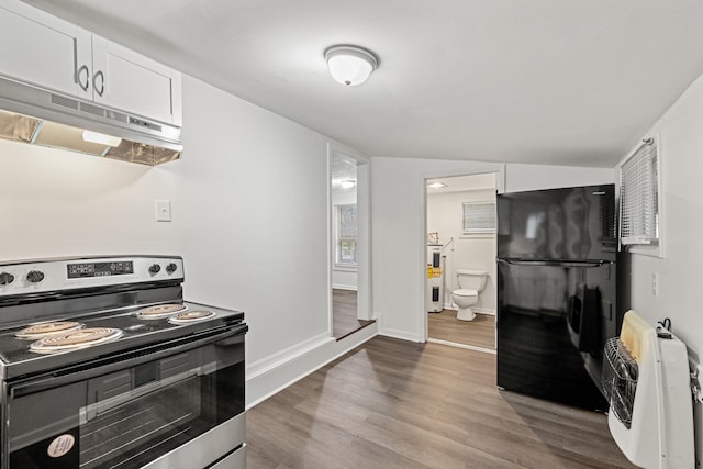 kitchen featuring black fridge, heating unit, electric range, white cabinetry, and range hood