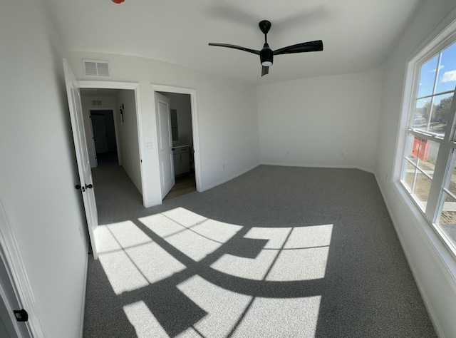 unfurnished bedroom with ceiling fan, ensuite bathroom, and dark carpet