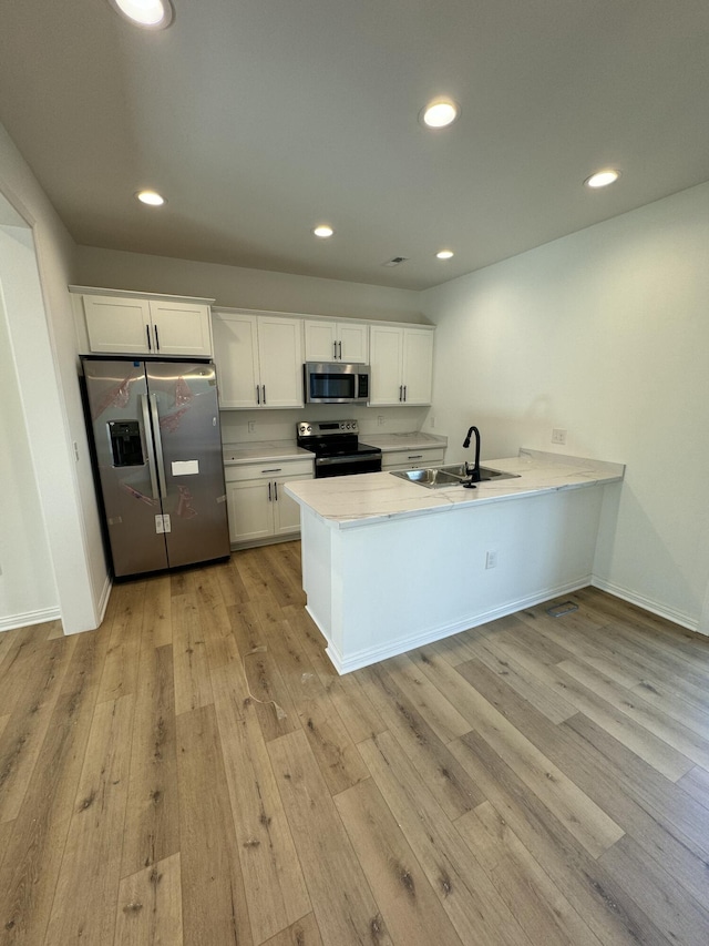 kitchen featuring sink, light hardwood / wood-style flooring, appliances with stainless steel finishes, white cabinetry, and kitchen peninsula