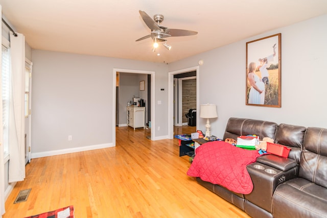 living area featuring baseboards, visible vents, ceiling fan, and wood finished floors