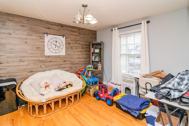 recreation room with wood walls, a notable chandelier, a textured ceiling, and wood finished floors