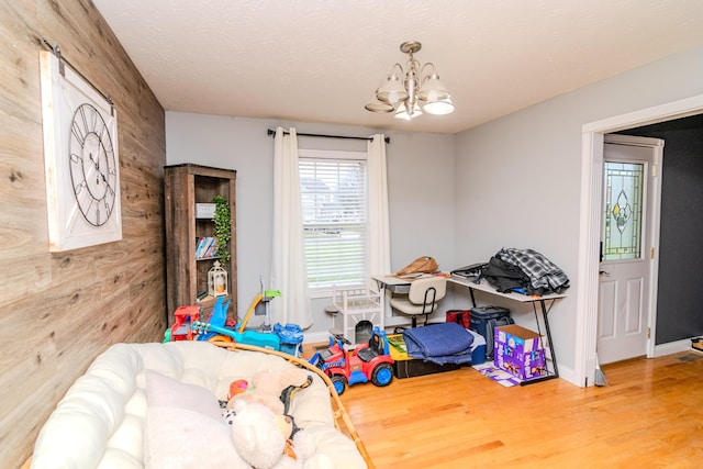 rec room with a textured ceiling, a notable chandelier, wood finished floors, and wooden walls