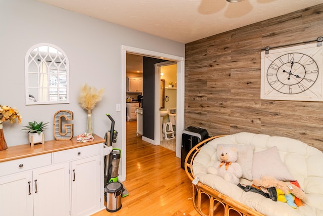 interior space featuring light wood finished floors, ensuite bath, wooden walls, and a textured ceiling