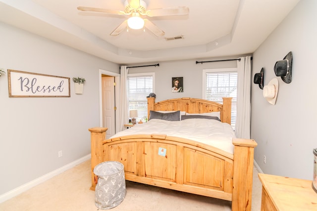 bedroom featuring a raised ceiling, multiple windows, visible vents, and baseboards