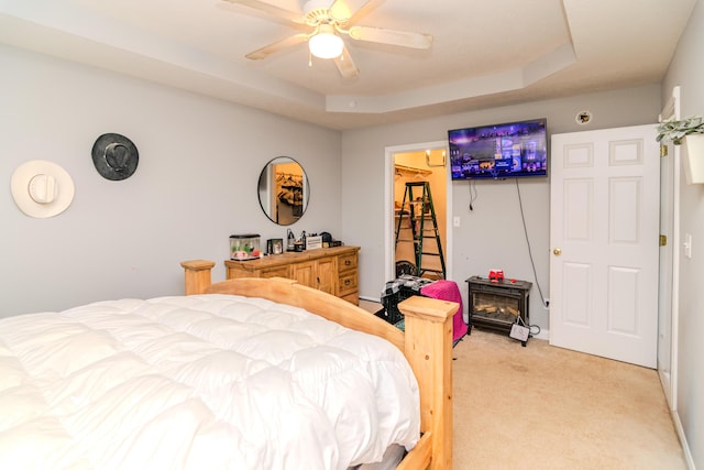 bedroom with a tray ceiling, a walk in closet, a ceiling fan, and light colored carpet