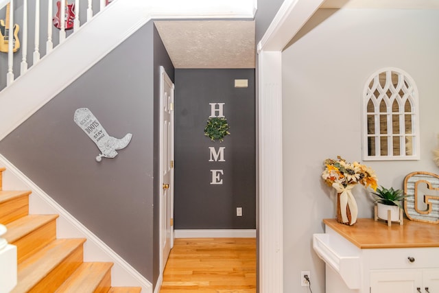 stairway featuring a textured ceiling, baseboards, and wood finished floors