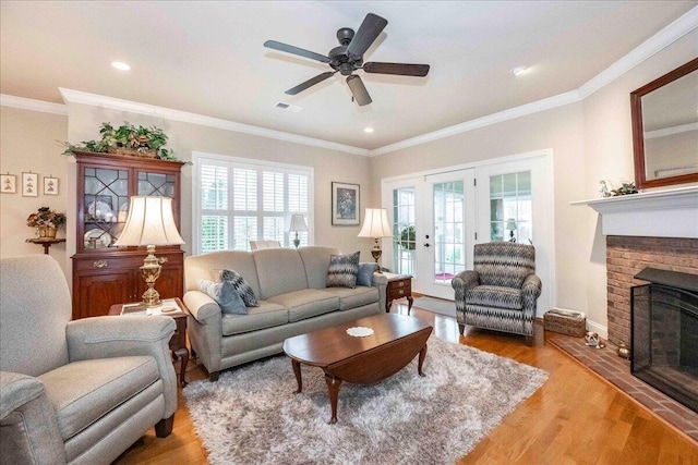 living room featuring ceiling fan, french doors, a brick fireplace, crown molding, and light hardwood / wood-style floors