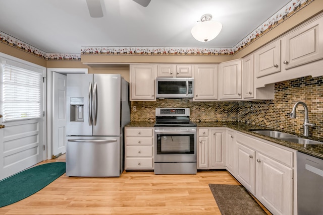 kitchen with sink, dark stone counters, light hardwood / wood-style floors, white cabinets, and appliances with stainless steel finishes