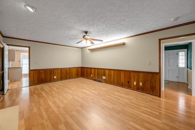 spare room with ornamental molding, a textured ceiling, ceiling fan, light hardwood / wood-style flooring, and wood walls