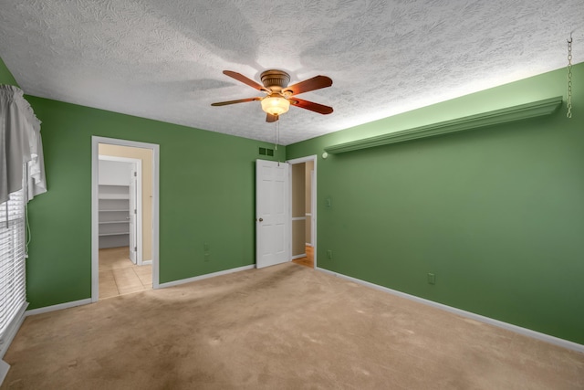 unfurnished bedroom with light carpet, a walk in closet, a textured ceiling, ceiling fan, and a closet