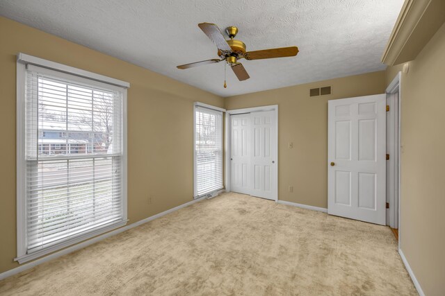 unfurnished bedroom with a textured ceiling, ceiling fan, light carpet, and a closet