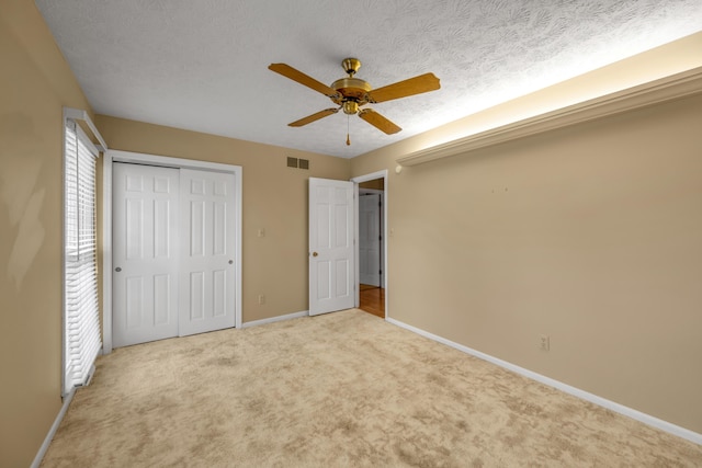 unfurnished bedroom with a textured ceiling, ceiling fan, light carpet, and a closet