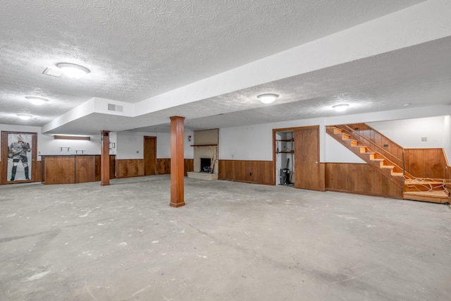 basement with a large fireplace, a textured ceiling, and wooden walls