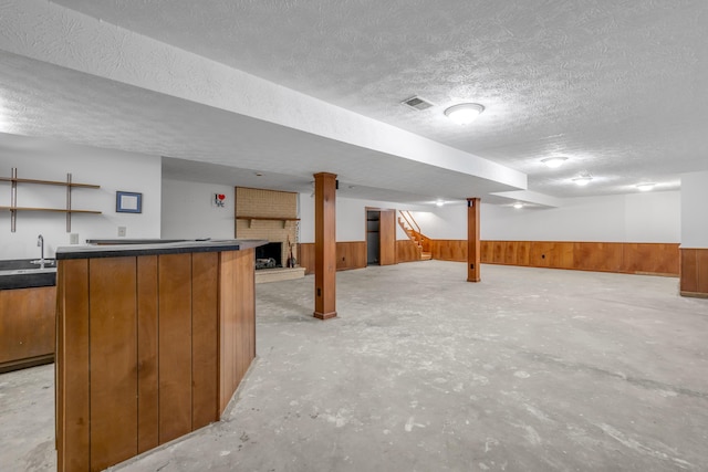 basement featuring wooden walls, a fireplace, a textured ceiling, and indoor wet bar