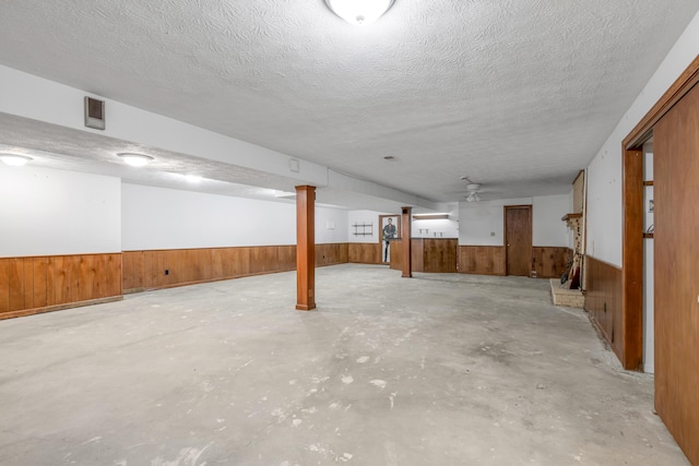 basement with wooden walls, ceiling fan, and a textured ceiling