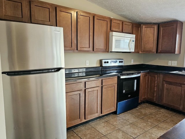 kitchen with lofted ceiling, electric range, stainless steel fridge, a textured ceiling, and light tile patterned flooring