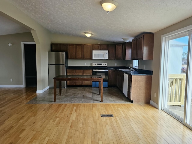 kitchen featuring a textured ceiling, light hardwood / wood-style flooring, lofted ceiling, and appliances with stainless steel finishes