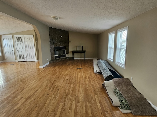 interior space with a tiled fireplace, lofted ceiling, light hardwood / wood-style floors, and a textured ceiling