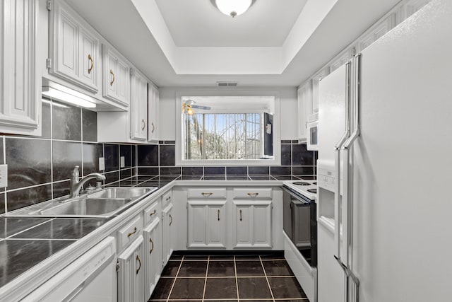 kitchen with a tray ceiling, sink, white appliances, and white cabinets