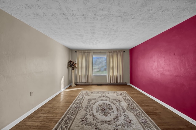 empty room with wood-type flooring, a textured ceiling, and a baseboard heating unit