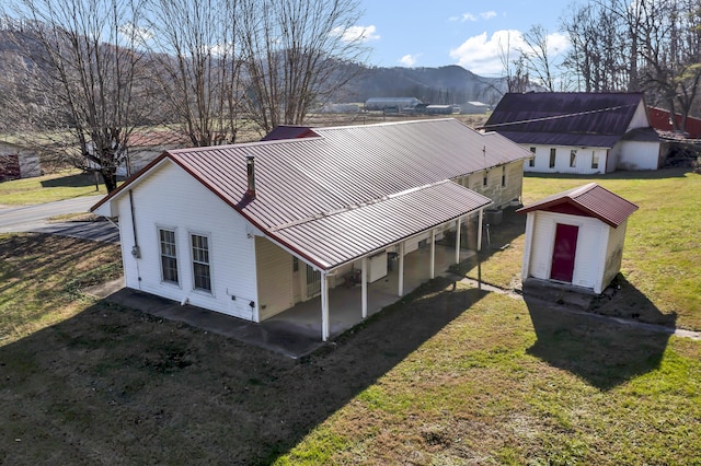 rear view of house featuring a mountain view, a yard, a patio, and a storage shed