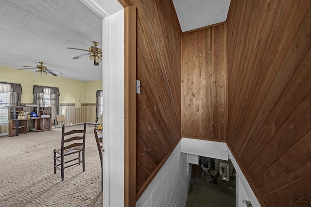 stairs with wood walls, carpet floors, and ceiling fan