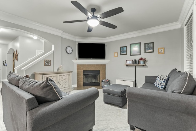 living room featuring ceiling fan, ornamental molding, and a tiled fireplace