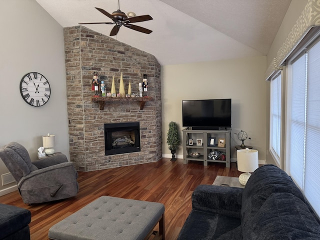 living room featuring dark hardwood / wood-style floors, ceiling fan, a stone fireplace, and vaulted ceiling