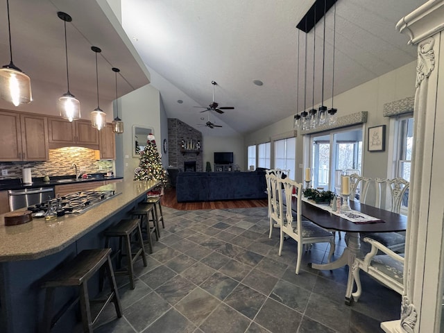 dining space featuring vaulted ceiling, ceiling fan, sink, a fireplace, and dark hardwood / wood-style floors