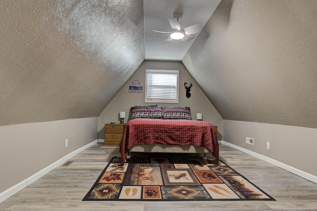 bedroom with a textured ceiling, ceiling fan, lofted ceiling, and light wood-type flooring