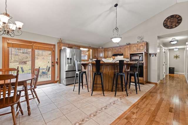 kitchen with a breakfast bar, an inviting chandelier, black appliances, vaulted ceiling, and light hardwood / wood-style floors