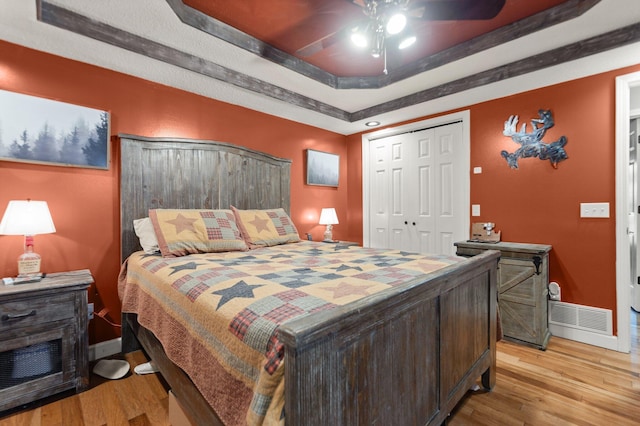 bedroom with ceiling fan, a raised ceiling, light wood-type flooring, and a closet