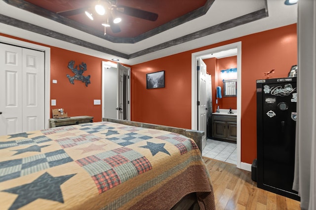 bedroom featuring ensuite bathroom, a tray ceiling, ceiling fan, light hardwood / wood-style floors, and a closet