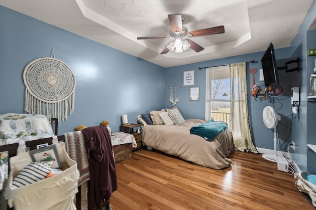 bedroom with a raised ceiling, ceiling fan, and hardwood / wood-style flooring