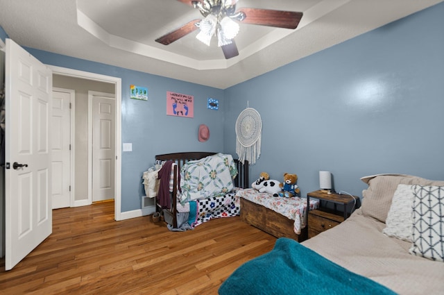 bedroom featuring hardwood / wood-style floors, ceiling fan, and a tray ceiling