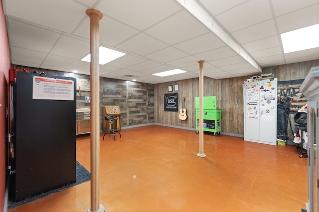 basement featuring a paneled ceiling, white refrigerator, and wooden walls