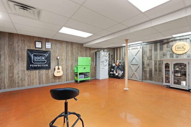 workout room with a paneled ceiling, a barn door, and wood walls