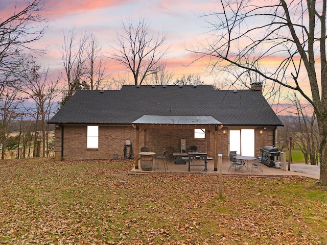 back house at dusk featuring a patio area and a yard