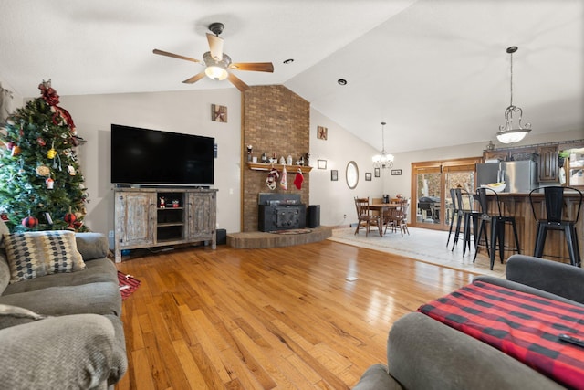 living room featuring lofted ceiling, wood-type flooring, ceiling fan with notable chandelier, and a wood stove