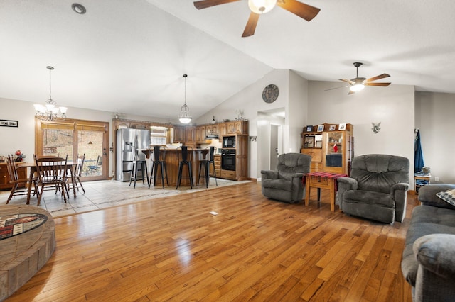 living room featuring high vaulted ceiling, light hardwood / wood-style floors, and ceiling fan with notable chandelier