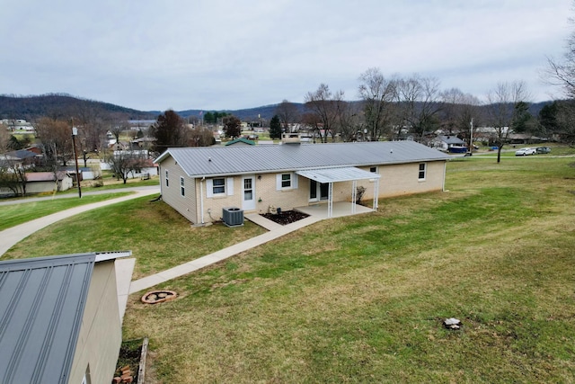 rear view of property with a lawn, a mountain view, central air condition unit, and a patio