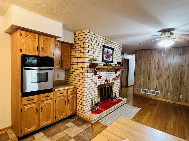 kitchen featuring dark hardwood / wood-style flooring, a brick fireplace, stainless steel oven, a textured ceiling, and wooden walls