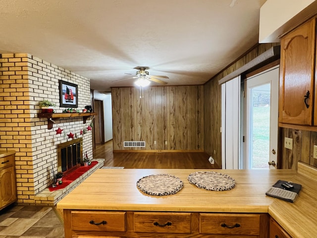 kitchen featuring a textured ceiling, ceiling fan, dark wood-type flooring, a fireplace, and wood walls