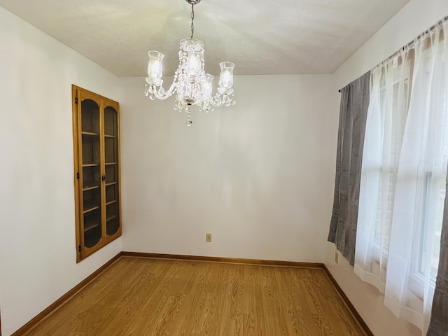 empty room with a wealth of natural light, wood-type flooring, a textured ceiling, and an inviting chandelier