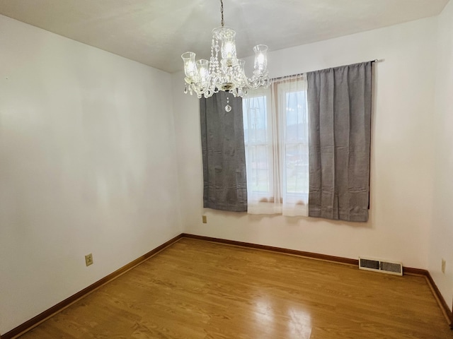 empty room featuring a chandelier and wood-type flooring