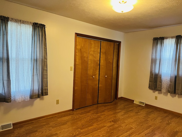 unfurnished bedroom featuring hardwood / wood-style floors, a textured ceiling, multiple windows, and a closet