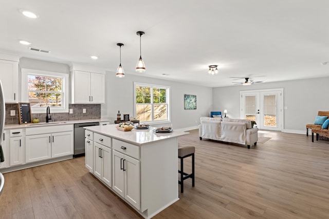 kitchen featuring a center island, white cabinets, light hardwood / wood-style flooring, stainless steel dishwasher, and decorative light fixtures