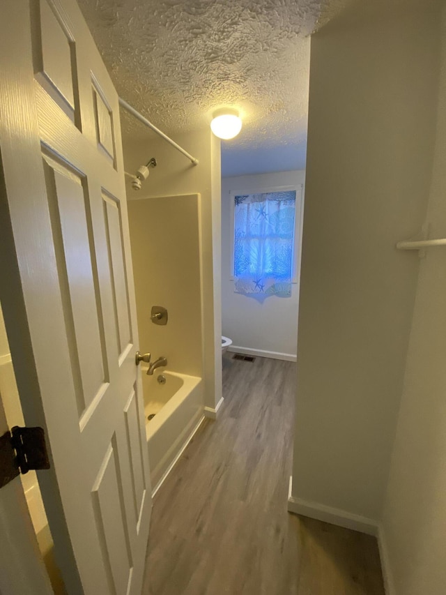 bathroom with toilet, wood-type flooring, a textured ceiling, and bathing tub / shower combination