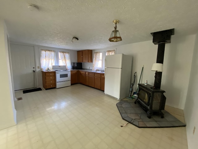 kitchen featuring a wood stove, sink, pendant lighting, a textured ceiling, and white appliances